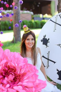 Young happy girl sitting at decorated place for children near big pink flower. Concept of beauty and festive decorations.