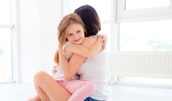 Mother with her little daughter girl tender hugging in light room