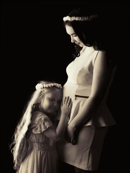 A little girl in the image of an angel hugs the belly of her eldest pregnant sister. The concept of family happiness, the birth of a child.