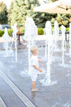 Little cute male baby standing near fountain. Concept of walking in city with children.