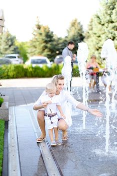 Young blonde mother sitting with little baby outside near fountain. Concept of walking in city and motherhood.