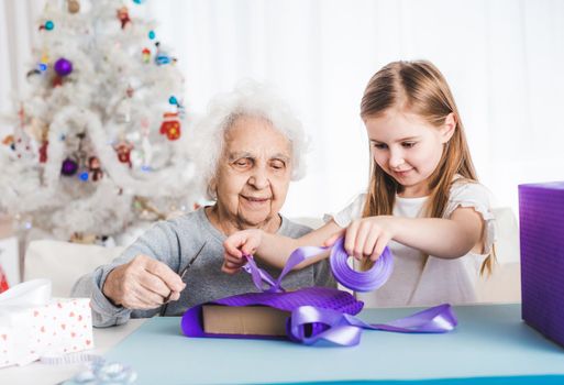 Smiling grandmother with little granddaughter decorating gifts together