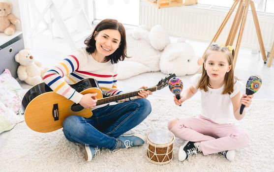 Beautiful woman playing guitar and singing with cute little girl