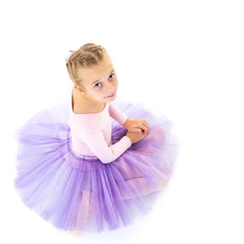 Charming little girl ballet dancer performing ballet poses on the floor in the studio on a white background.Isolated.