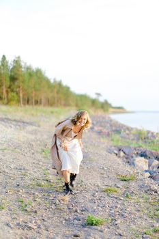 Caucasian young girl walking on shingle beach and wearing summer coat. Concept of seasonal fashion and summer vacations.