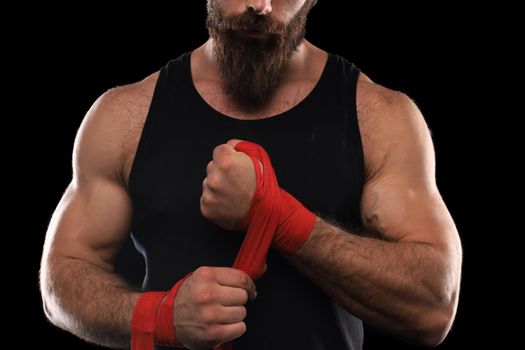 Athlete stands in black clothes and wraps his hands in red textile elastic bandage before training