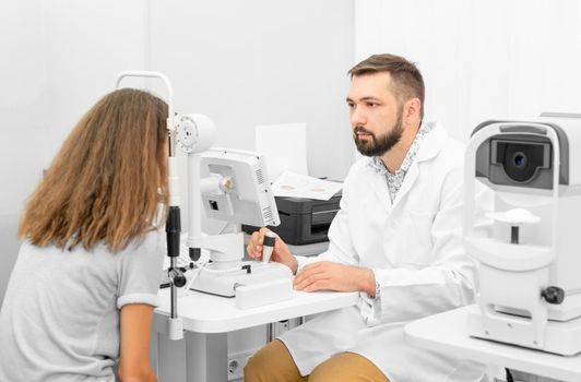 Doctor ophthalmologist holding equipment examinating teenager girl's eyes in the clinic