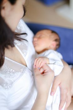 Young mother wearing white clothes holding newborn baby. Concept of motherhood and happiness.