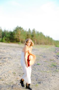 Caucasian european girl walking on rocky beach with hant in hands and wearing dress. Concept of summer vacations and fashion.