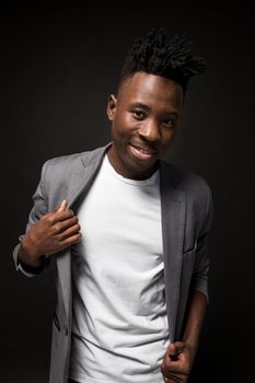 Close-up portrait of handsome black man with charming smile. Studio shot of well-dressed african guy wears white T-shirt and gray jacket, on dark background