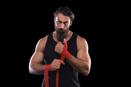 Athlete stands in black clothes and wraps his hands in red textile elastic bandage before training