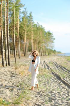 Female person walking on sand beach and wearing white clothes. Concept of summer vacations.