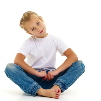 A cute little girl is sitting on the floor, wearing a clean white T-shirt and jeans. On the shirt you can put a logo or any other inscription. The concept of advertising on clothes, Happy childhood. Isolated on white background.