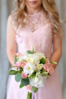 Happy bride keeping bouquet of flowers and wearing light pink dress. Concept of wedding photo session and floristic art.