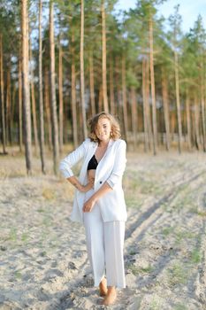 Blonde european girl walking on sand beach and wearing white clothes. Concept of summer vacations.