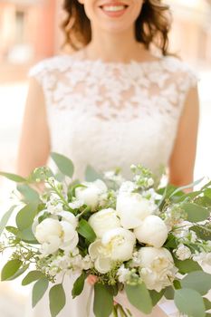 Happy fiancee keeping bouquet of flowers and wearing white dress. Concept of bridal photo session and wedding.