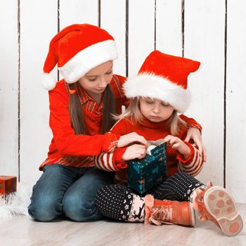 two little girls in red hats sitting on the floor with gifts near new year tree