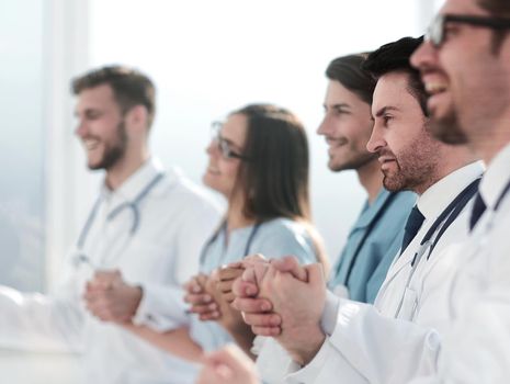 Happy group of people in white coats holding hands during a conference call.