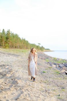 Caucasian girl walking on shingle beach and wearing summer coat. Concept of seasonal fashion and summer vacations.