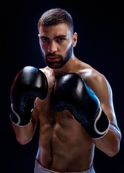 Strong muscular boxer in black boxing gloves. A man in a boxing stand on black background. Strength and motivation. Studio shot