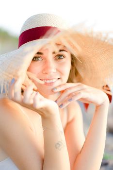 Portrait of beautiful woman wearing hat sitting on sand beach. Concept of fashion, beauty and summer vacations.