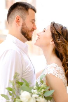 Happy groom hugging bride keeping bouquet of flowers. Concept of love and wedding photo session.