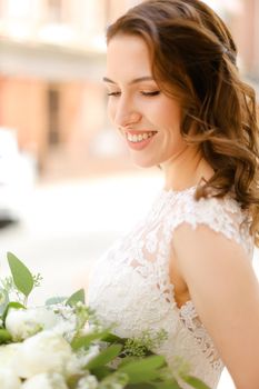 Happy beautiful fiancee keeping bouquet of flowers and wearing white dress. Concept of bridal photo session and wedding.