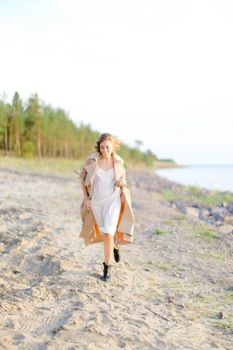 Caucasian beautiful girl walking on shingle beach and wearing summer coat. Concept of seasonal fashion and summer vacations.