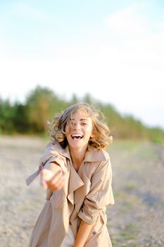 Caucasian girl with outstretched hand on shingle beach wearing summer coat. Concept of seasonal fashion and summer vacations.