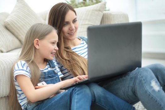 mom and daughter sitting on the carpet in the living room and using a laptop.photo with copy space