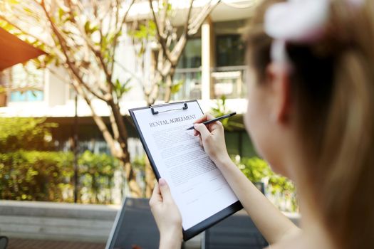 girl travel and rent short term condo in europe. concept of traveler looking for place to live sunny day, focus on doc. close up portrait of woman hands signing rental agreement on background of leasing office apartments. Front used with Open Font License