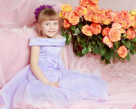 Fashionable little girl in a stylish beautiful dress.The girl sits on a luxurious pink armchair near a large bouquet of tea roses.