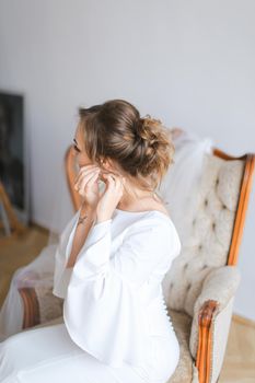 Young bride dressing earrings. Concept of wedding preparing in morning.