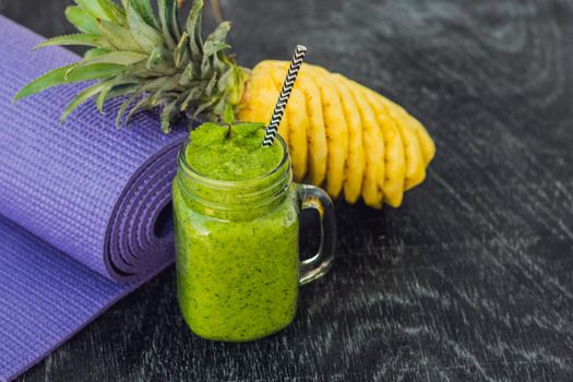 Green smoothies made of spinach and pineapple and a yoga mat. Healthy eating and sports concept.