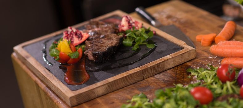 Juicy slices of grilled steak  with vegetables on a wooden board