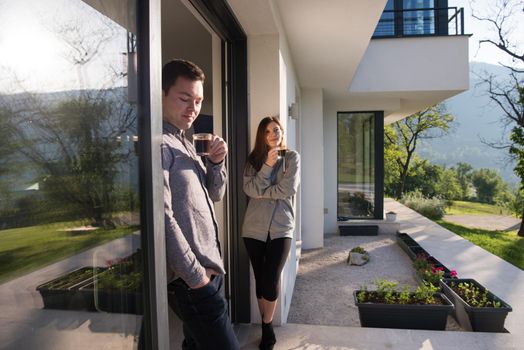 young beautiful handsome couple enjoying morning coffee on the door of their luxury home villa