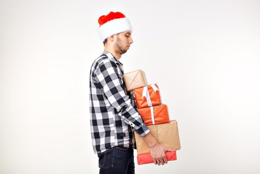 Holidays and presents concept - Funny man in Christmas hat holding many gift boxes on white background.