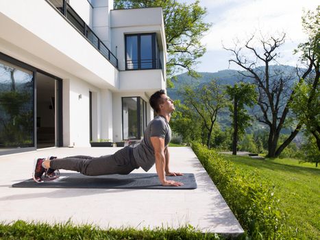 young handsome man doing morning yoga exercises in front of his luxury home villa