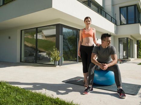 young beautiful woman and personal trainer doing exercise with pilates ball in front of her luxury home