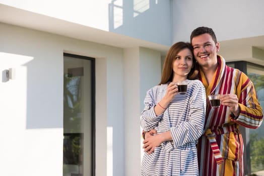 Young beautiful couple in bathrobes are enjoying morning coffee in front of their luxury home villa