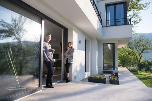 young beautiful handsome couple enjoying morning coffee on the door of their luxury home villa