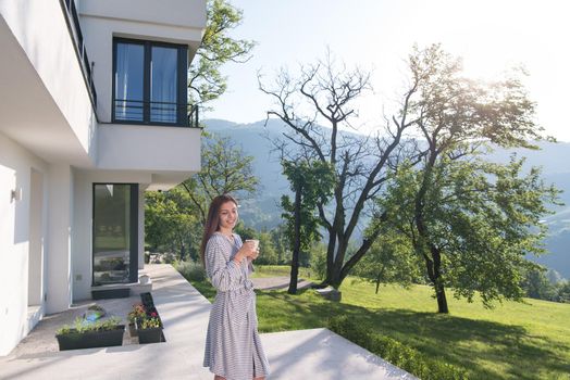 young beautiful woman in a bathrobe enjoying morning coffee in front of her luxury home villa