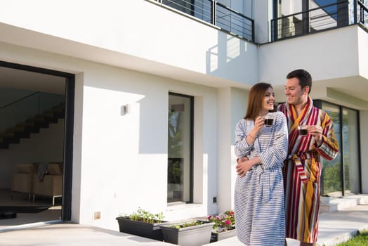 Young beautiful couple in bathrobes are enjoying morning coffee in front of their luxury home villa