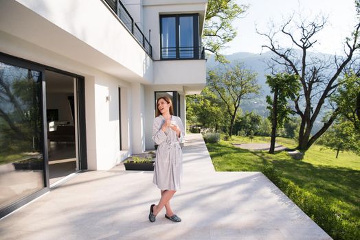 young beautiful woman in a bathrobe enjoying morning coffee in front of her luxury home villa