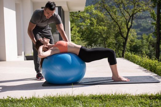 young beautiful woman and personal trainer doing exercise with pilates ball in front of her luxury home