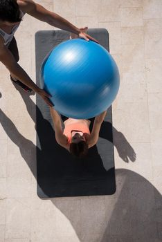 young beautiful woman and personal trainer doing exercise with pilates ball in front of her luxury home