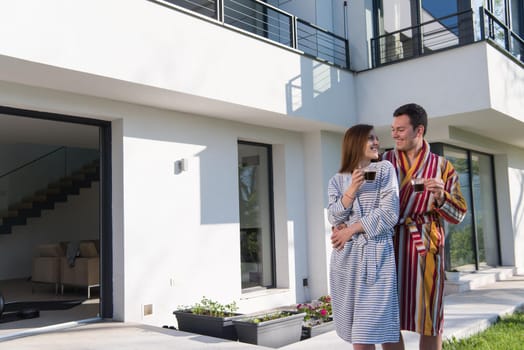 Young beautiful couple in bathrobes are enjoying morning coffee in front of their luxury home villa