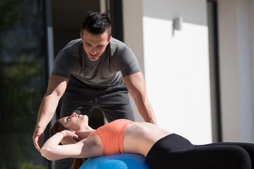 young beautiful woman and personal trainer doing exercise with pilates ball in front of her luxury home