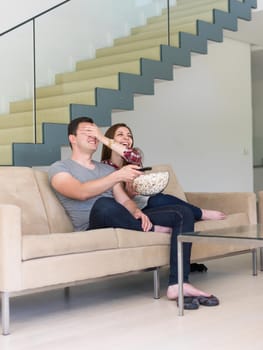 young handsome couple enjoying free time watching television with popcorn in their luxury home villa