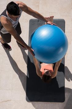 young beautiful woman and personal trainer doing exercise with pilates ball in front of her luxury home